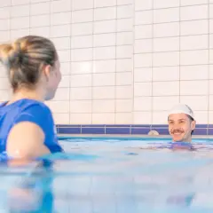 Uśmiechnięty mężczyzna w czepku pływackim i kobieta w niebieskiej koszulce w basenie, ćwiczący metodę Halliwick.