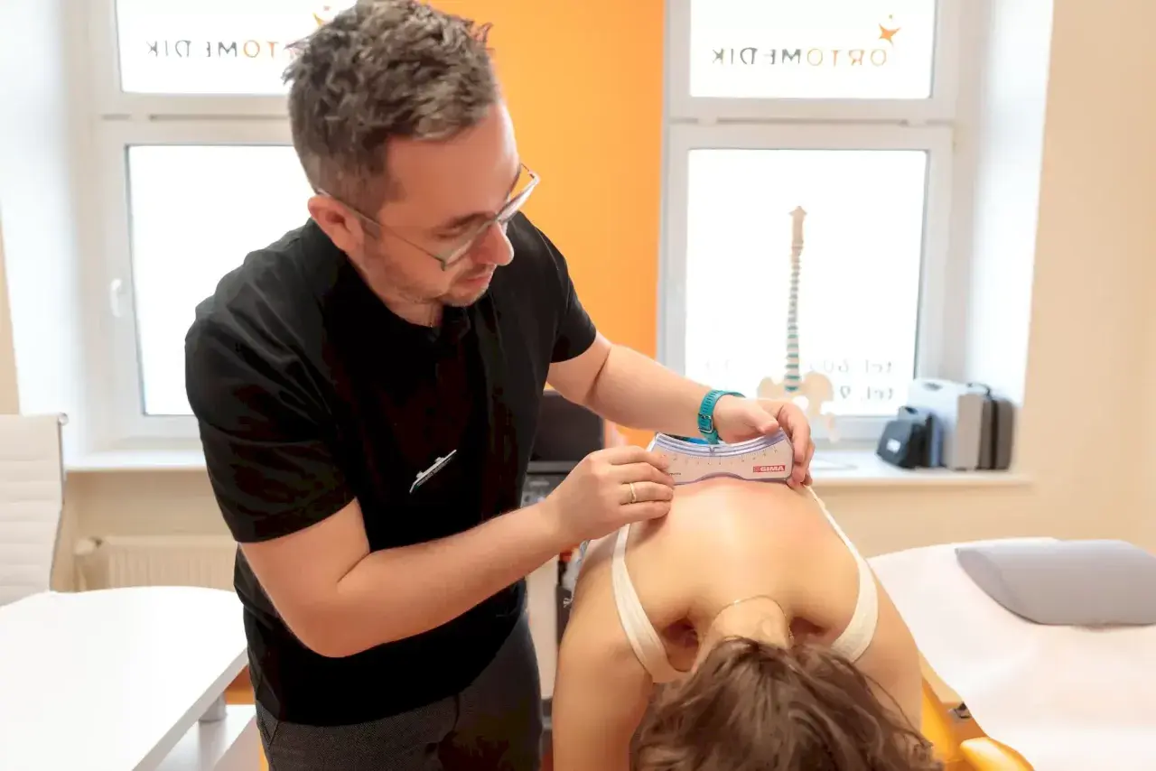 Fizjoterapeuta wykonuje diagnostykę funkcjonalną kręgosłupa pacjentki przy użyciu goniometru.