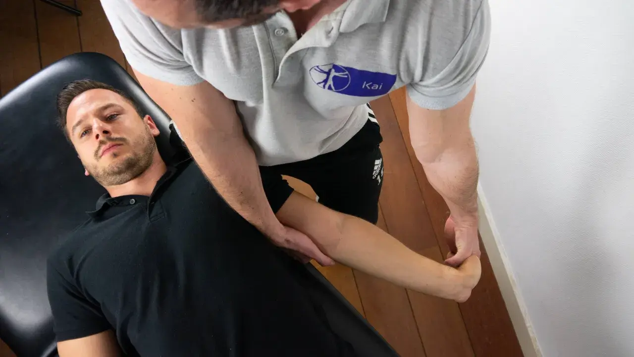 Fizjoterapeuta wykonuje test lovetta kończyny górnej u pacjenta leżącego na kozetce.