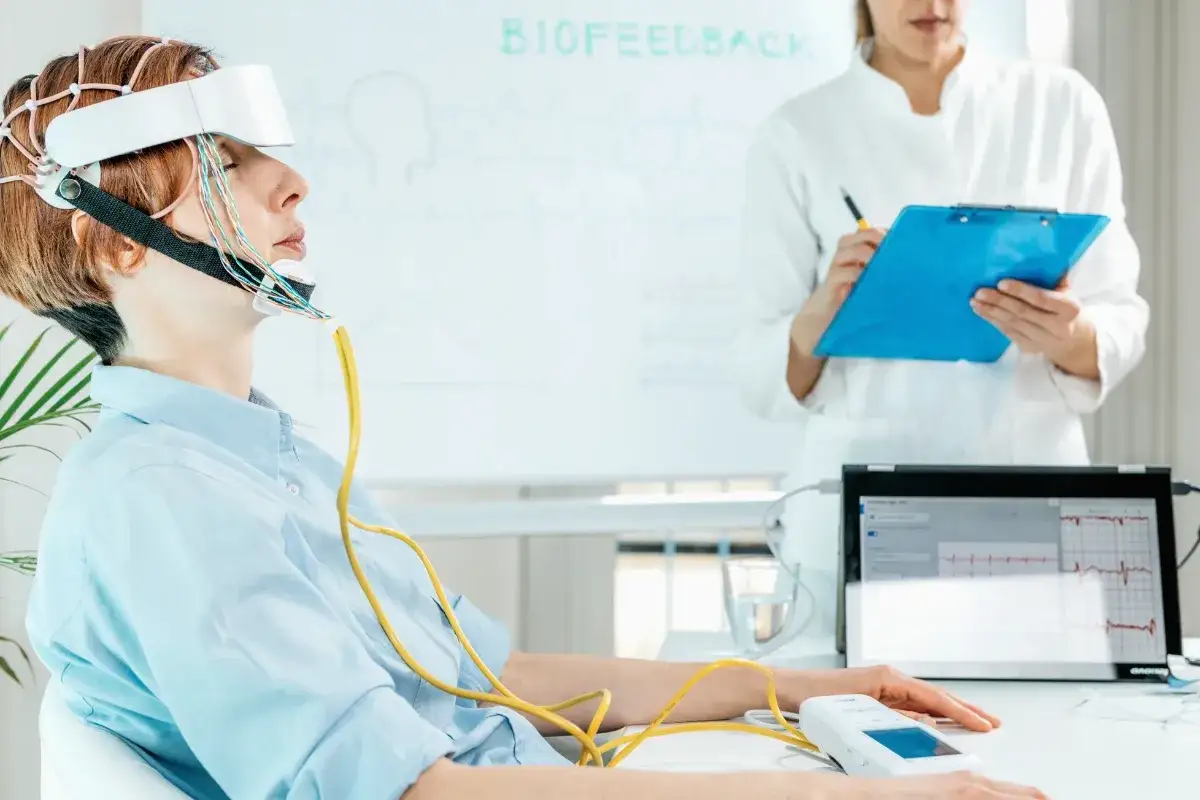 Kobieta z elektrodami na głowie uczestniczy w badaniu metodami neurofizjologicznymi. Obok niej monitor z zapisem fal mózgowych.