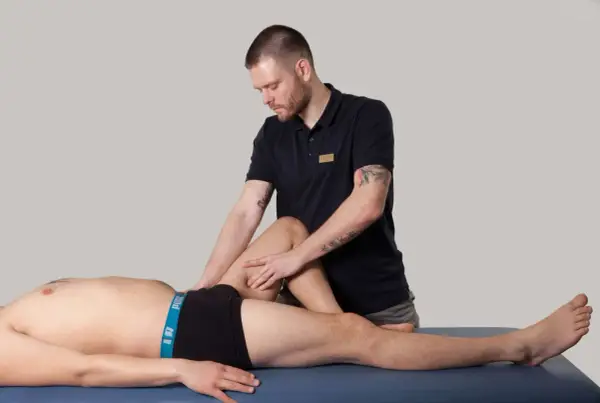 Fizjoterapeuta pracuje z mięśniami kończyny dolnej pacjenta, wykonując masaż.